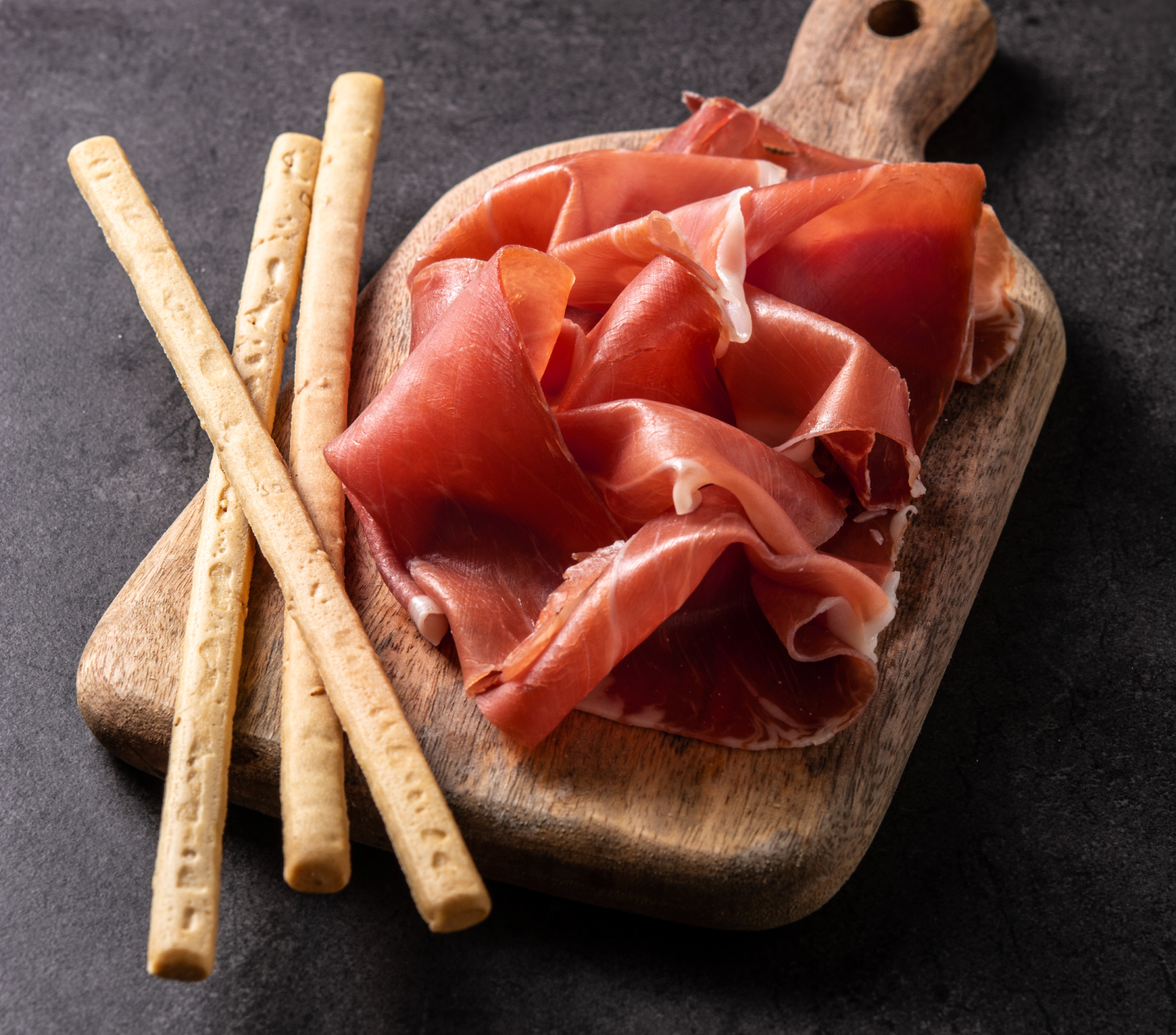 Jamón en lonchas sobre tabla con picos de pan